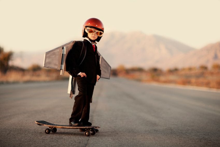 boy in suite on skateboard with jetpack, helmet, and giant goggles looking at the camera